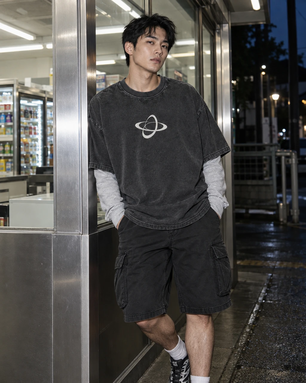 Actual Foltara night streetwear study: washed graphic tee layered over grey sleeves beside a shop